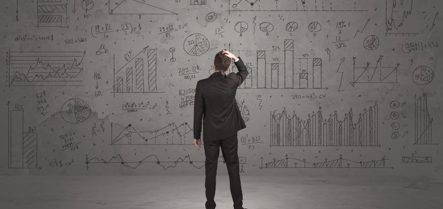 A successful confident businessman thinking about decisions, standing in front of wall full with graph pie charts and calculations concept