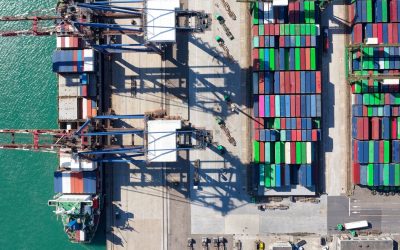 Vertical top down view of cargo containers piled on the quayside and cranes unloading the goods from a ship, which is parking at the dock of Taipei Harbor in Bali District, New Taipei City, Taiwan