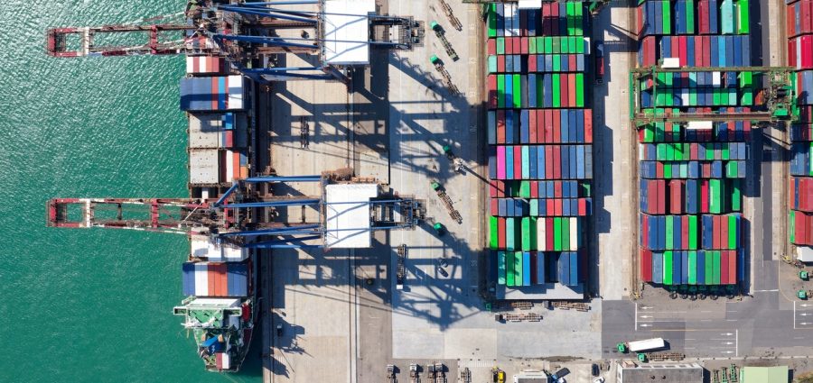 Vertical top down view of cargo containers piled on the quayside and cranes unloading the goods from a ship, which is parking at the dock of Taipei Harbor in Bali District, New Taipei City, Taiwan