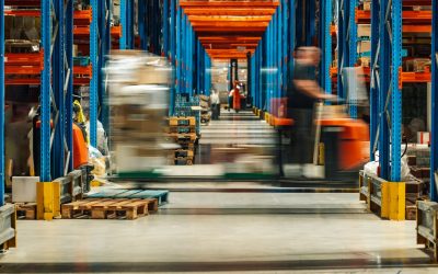 Warehouse workers are operating forklifts, transporting goods between tall shelves filled with various products, showcasing the fast paced environment of a modern distribution center