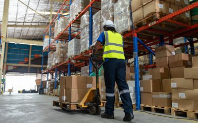 African American man worker using pallet truck for move cardboard boxes. Storehouse employee in uniform working and unloading goods in warehouse. Logistics, Distribution Center concept.