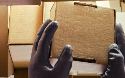 A worker man hands hold cardboard boxes on the shelves of a fully stocked warehouse. Warehouse overflowing with boxes of goods and postal parcels