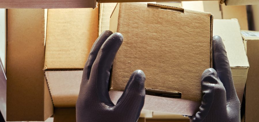 A worker man hands hold cardboard boxes on the shelves of a fully stocked warehouse. Warehouse overflowing with boxes of goods and postal parcels