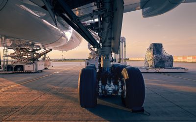 Landing gear of large plane. Preparation cargo airplane before flight at beautiful sunset. Unloading and loading of freight containers at airport.