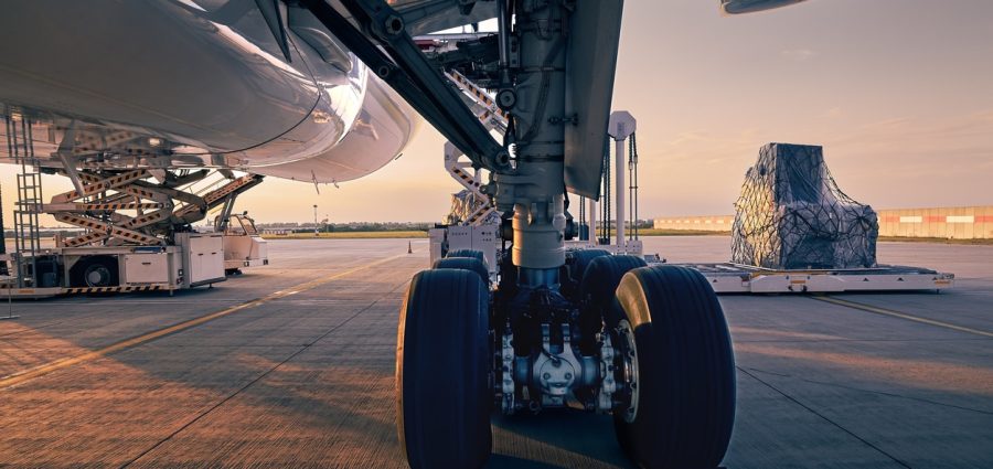 Landing gear of large plane. Preparation cargo airplane before flight at beautiful sunset. Unloading and loading of freight containers at airport.