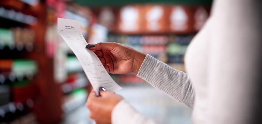 Woman Checking Grocery Store Receipt After Shopping At Supermarket Aisle. Possible Professions: Cashier, Accountant