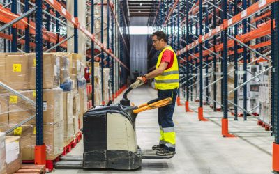 Warehouse worker driving a forklift between aisles of packaged goods, managing logistics and distribution in a large storage facility