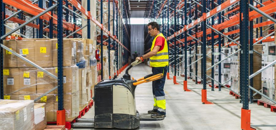 Warehouse worker driving a forklift between aisles of packaged goods, managing logistics and distribution in a large storage facility